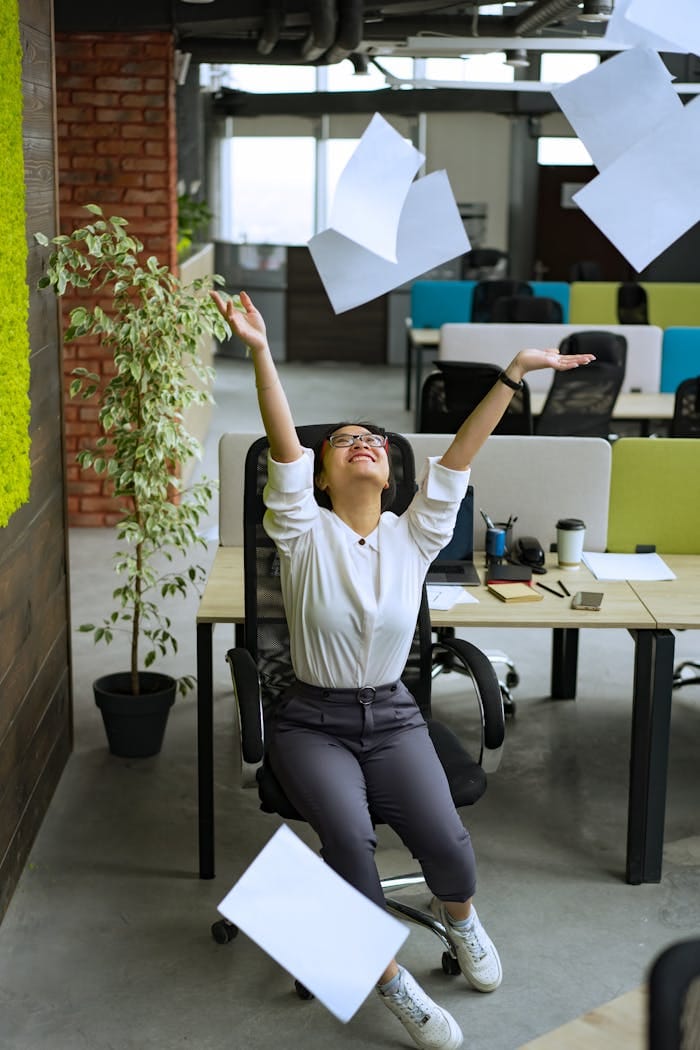 A delighted woman throws papers in the air, celebrating in a contemporary office setting.